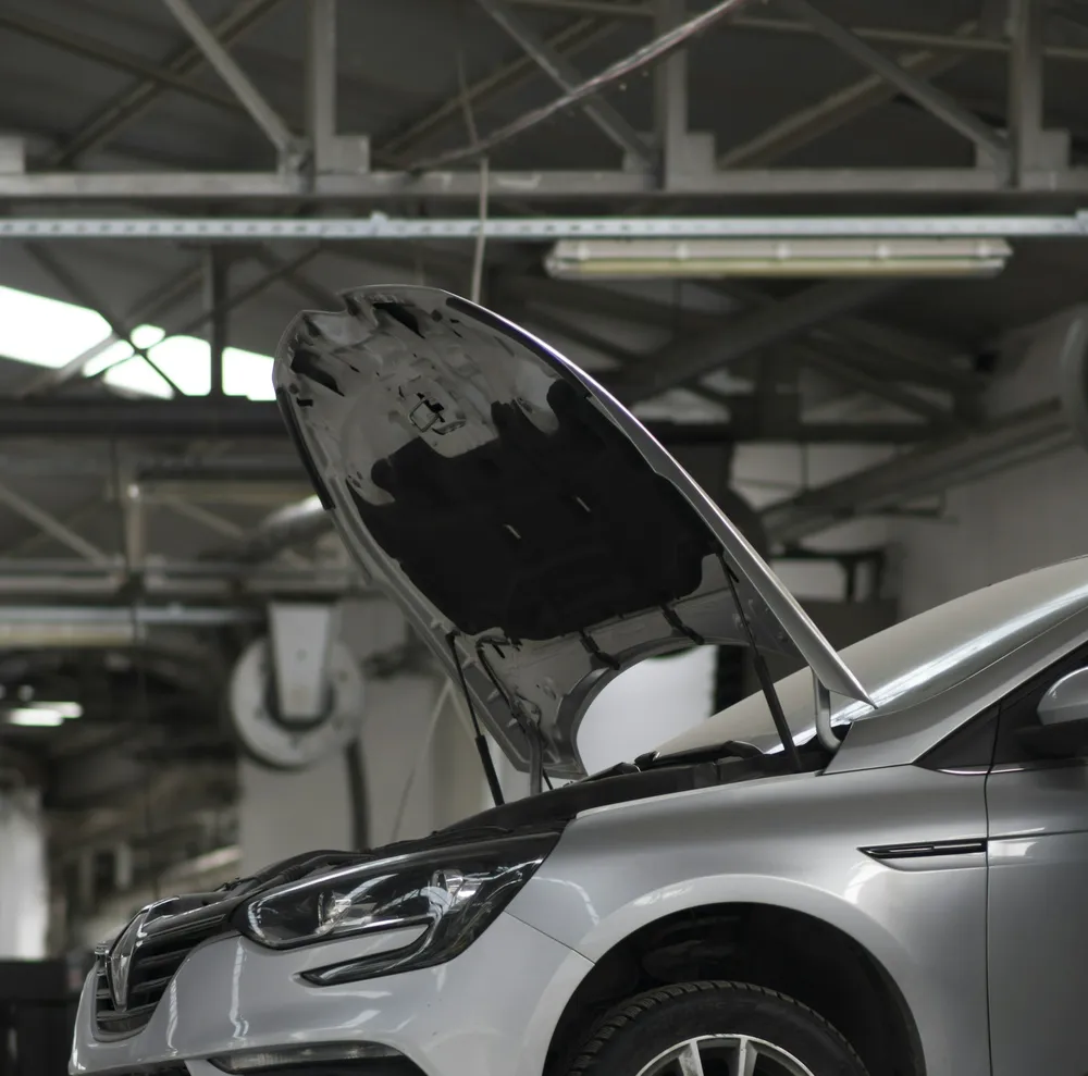 A silver car with its hood open in a clean service bay