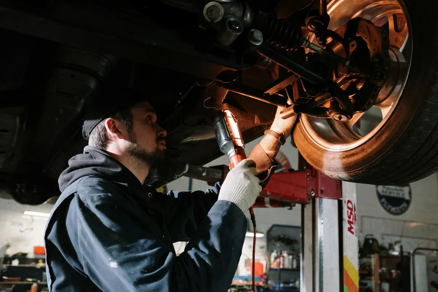 Mechanic inspecting the underside of a lifted car with a work light