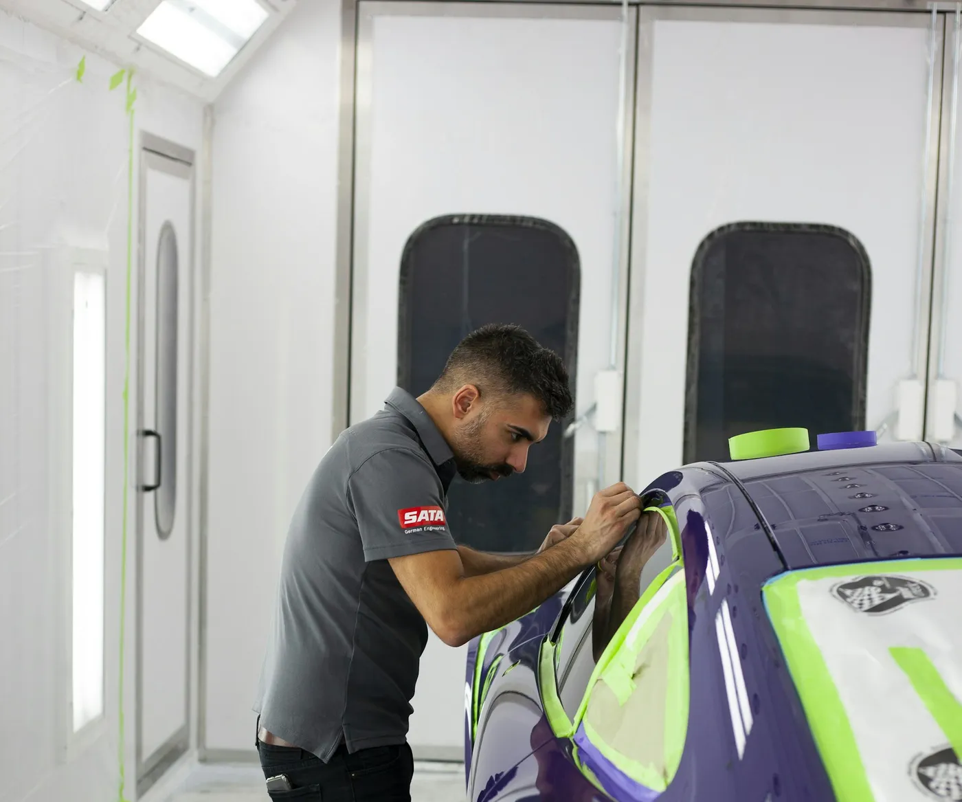 Technician masking a car for paint in a bright paint booth