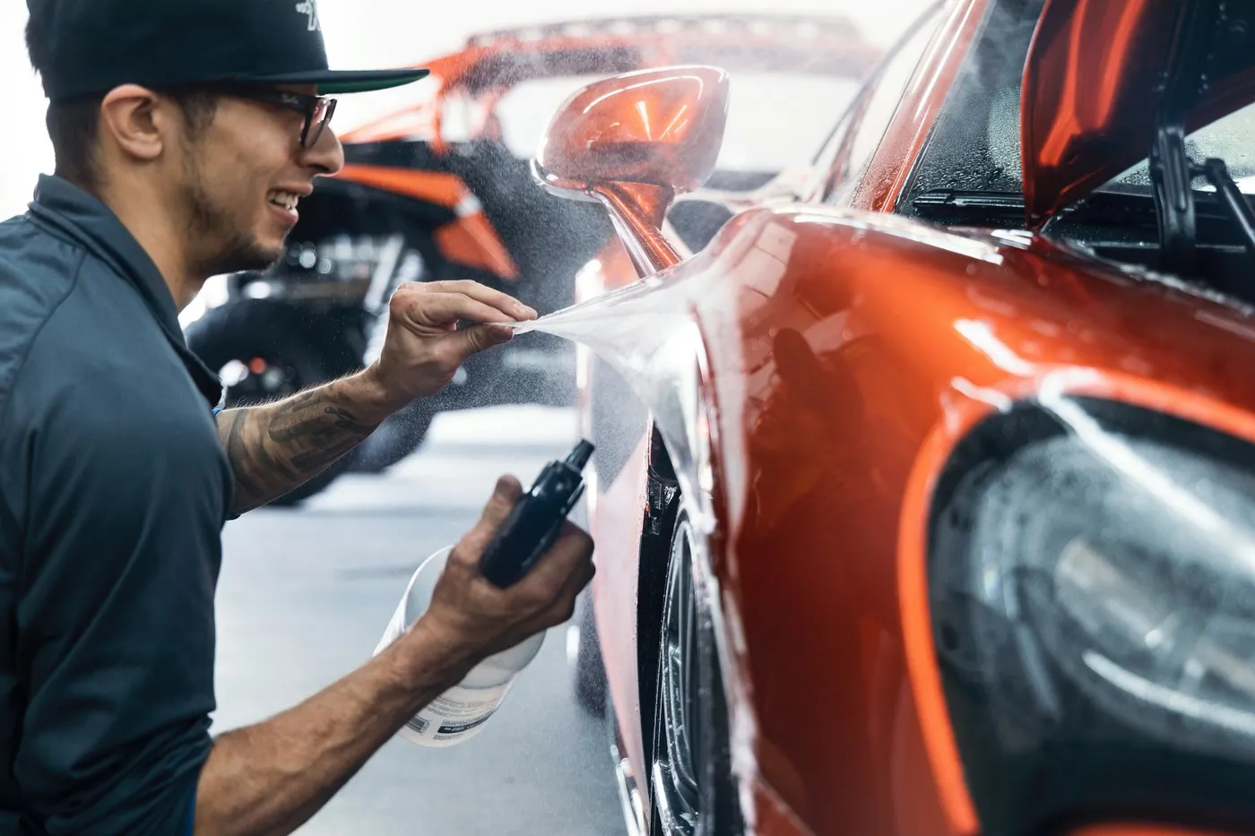 Smiling technician detailing the fender of an orange car