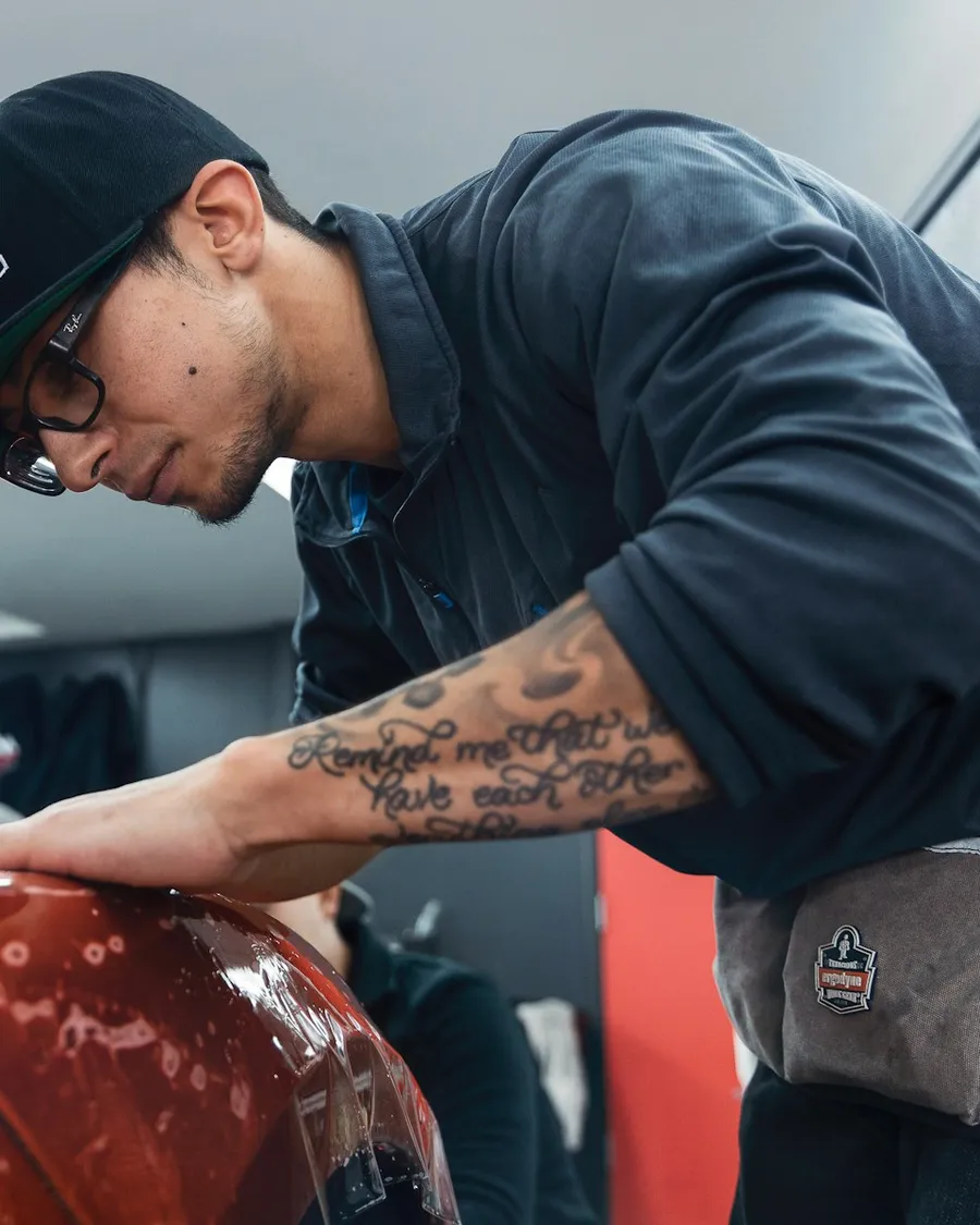 Technician working on the fender of an orange car in a bright shop